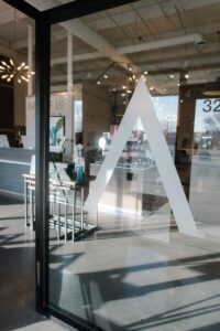 Glass door with a white "A" logo at the entrance to the best salon in Waukee/Urbandale, offering balayage, bridal hair, highlights, hair extensions, and permanent jewelry.