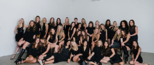 A team of women in black, stylists at the best salon in Waukee and Urbandale, pose together—balayage, highlights, hair extensions.