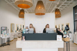 At the Art of Life Salon, voted best salon in Waukee and Urbandale, staff greet clients for balayage, highlights, extensions, bridal hair, and permanent jewelry; modern stations and mirrors line the stylish space.