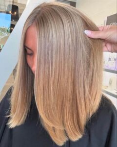 A client at the best salon in Waukee shows off shoulder-length, blonde balayage highlights while getting hair extensions applied.