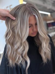 At the best salon in Waukee or Urbandale, a stylist showcases balayage, highlights, and hair extensions on ash-blonde hair.