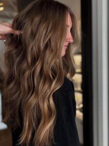 A woman with balayage highlights and long, wavy hair, seen in profile at the best salon in Waukee or Urbandale, gets her hair lifted.
