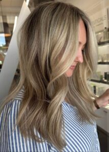 A woman with balayage and blonde highlights from the best salon in Waukee wears a striped shirt, perfect for bridal hair inspo.