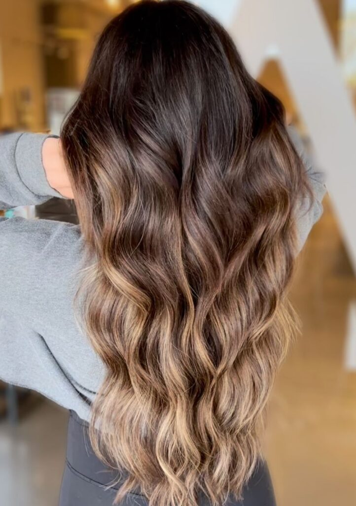 - Art of Life Salon & Spa at Urbandale and Waukee, IA A person with balayage and highlights in long, wavy brown hair at the best salon in Waukee or Urbandale, hands to their head. - Art of Life Salon & Spa at Urbandale and Waukee, IA
